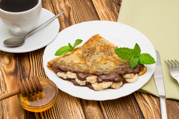 Crepes with bananas and cream on a wooden background
