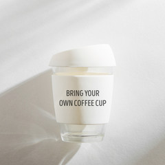 White reusable eco coffee cup on white morning background.