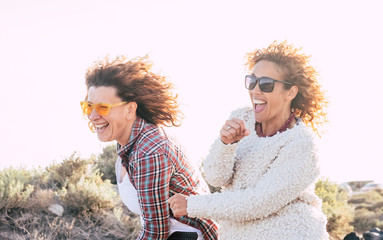 Two playful happy cheerful middle age women have lot of fun playing together - craziness and playful concept for nice people in outdoor - white sky background and bright image