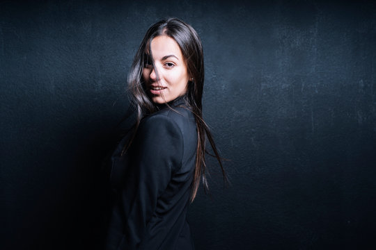 Portrait of young woman wearing black blazer in front of black background