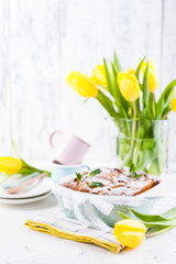Apple pie in dishes on a white background and a bouquet of spring yellow tulips. Homemade pastries with fruit for a delicious breakfast Easter breakfast. Free space for text. Copy space.