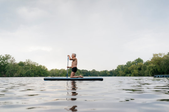 Senior man kneeling on SUP board - Powered by Adobe