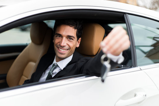 Young businessman smiling in his new car showing car keys