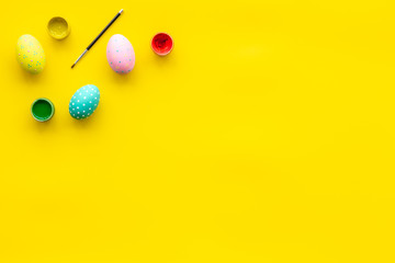 Colorful Easter eggs and paint for celebration on yellow background top view mock up