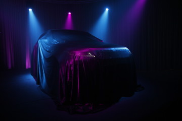 Car covered with dark cloth on a black background 
