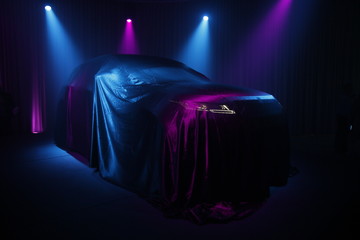 Car covered with dark cloth on a black background 