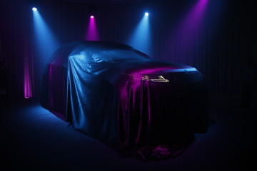 Car covered with dark cloth on a black background 
