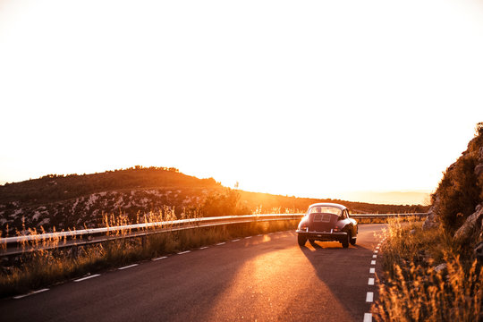 Spain, Classic Car Driving On Road During Sunset