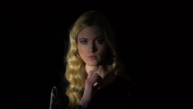 Sexy blond female showing silence gesture against dark background, seduction
