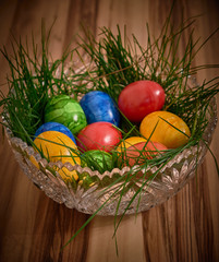 Ostereier in einer Kristallschüssel in grünem Gras mit einem Hintergrund aus Nussbaum und dunkler Vignette.