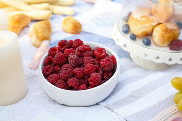 White bowl with fresh raspberry on white picnic blanket