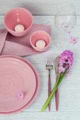 Pink rustic place setting with purple hyacinth flower, candles and linen napkin on white wooden background