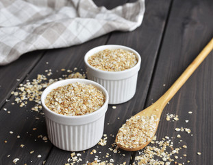 Rolled oats in bowls and spoon on dark wooden table background