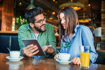 Young couple having fun with tablet in a cafe. Love, dating, lifestyle, technology concept