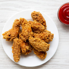 Chicken wings on a round white plate with ketchup over white wooden surface, top view. Overhead, flat lay, from above. Closeup.