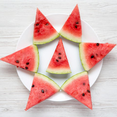 Creative layout of chopped watermelon on white plate over white wooden surface, top view. Flat lay, overhead, from above.