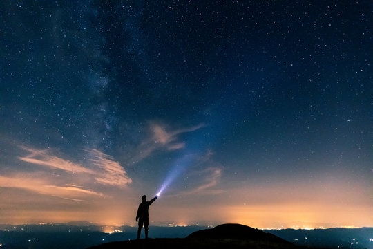 Italy, Monte Nerone, silhouette of a man with torch under night sky with stars and milky way