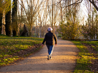 Fototapeta premium A senior woman with white hair listening to music with headphones walking in an urban park