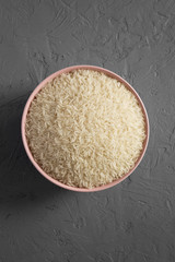 Dry white rice basmati in a pink bowl over concrete surface, top view. Flat lay, overhead, from above.