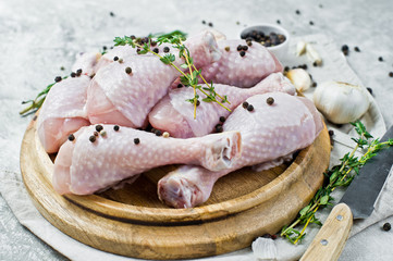 Raw chicken legs. Ingredients for cooking: rosemary, thyme, garlic, pepper. Gray background, side view.
