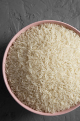 Dry white rice basmati in a pink bowl over gray background, top view. Flat lay, overhead, from above. Close-up.