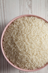 Dry white rice basmati in a pink bowl over white wooden background, overhead view. Flat lay, top view, from above.