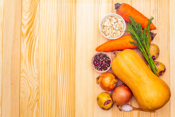 Fresh ingredient for pumpkin soup. Pumpkin, onion, carrot, potato, spices, seeds, pepper mix, salt, dill. Vegetables on wooden background, top view.