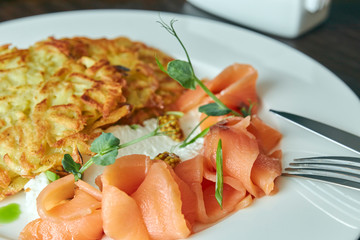 dish Marinated salmon with dill and potato pancakes on a wooden table. fresh salted trout. dish on a plate. Russian food. horizontal view.