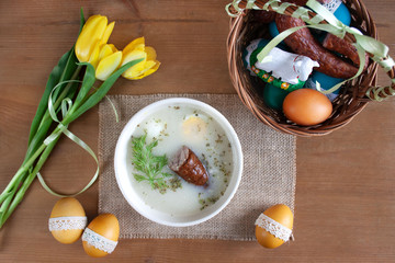 Śniadanie wielkanocne - barszcz biały z jajkiemi i kiełbasą, obok pisanki i koszyczek ze święconką