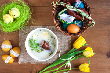 Śniadanie wielkanocne - barszcz biały z jajkiemi i kiełbasą, obok pisanki i koszyczek ze...