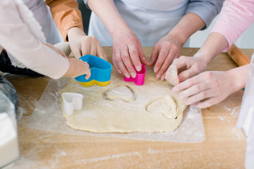 Two sisters, grandmother and little baby daughter are cooking in the kitchen to Mothers day, lifestyle photo series in bright home interior. Hands cutting hearts cookies from dough fom mother's day