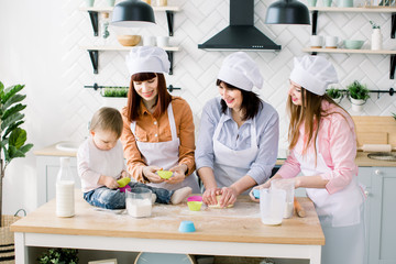 Two sisters, grandmother and little baby daughter are cooking in the kitchen to Mothers day, lifestyle photo series in bright home interior