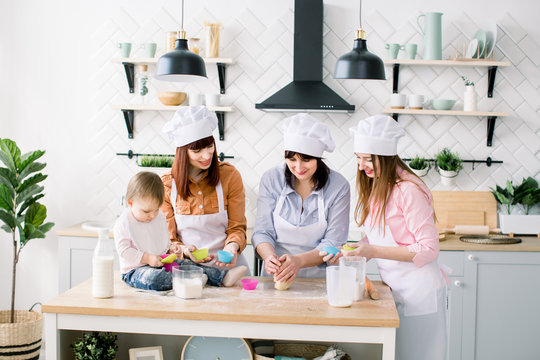 Happy family in the kitchen. Young woman and her sister, middle aged woman and little cute daughter cooking cupcakes for Mothers day, casual lifestyle photo series in real life interior