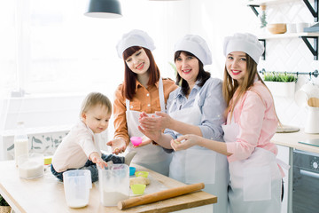 Little baby girl helps to make cupcakes together with mother, aunt and grandmother. Pretty women...