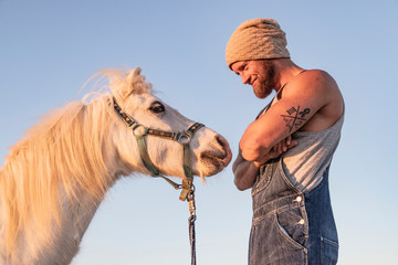 Smiling man facing pony under blue sky