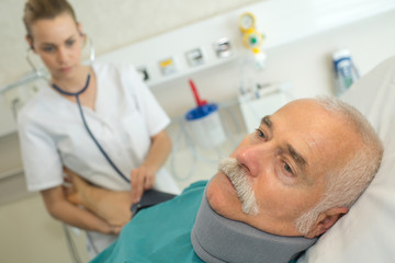 nurse taking blood pressure of mature patient wearing neck brace