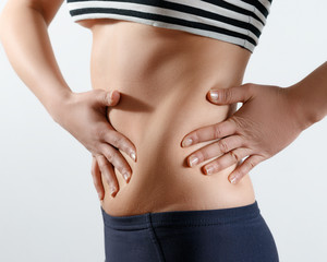 a young slender beautiful girl stands sideways and feels her back, waist and stomach with her...