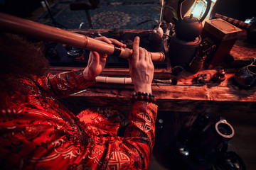 Chinese tea ceremony. Tea master in kimono performs in the dark room with a wooden interior, playing on a bamboo flute. Tradition, health, harmony.