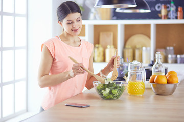 Smiling young woman mixing fresh salad in the kitchen.