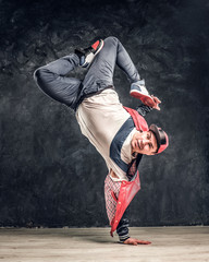 Hip-hop style dancer performs breakdance acrobatic elements. Studio photo against a dark textured...