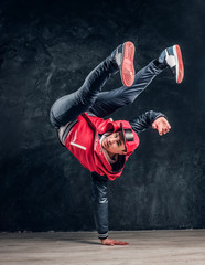 Hip-hop style dancer performs breakdance acrobatic elements. Studio photo against a dark textured wall