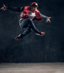 Fototapeta na wymiar Emotional hip-hop style dancer performing dance elements. Studio photo against a dark textured wall