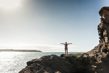Young woman hiking on a rocky beach, looking at view