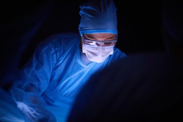 Doctor performing surgery in a dark background.