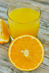 A glass of fresh orange juice and orange fruits on a wooden table. vertical view close-up. refreshing citrus drink.