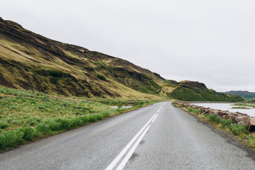 The road between the mountains and the hills. Asphalt road in Iceland. The road is in the field.