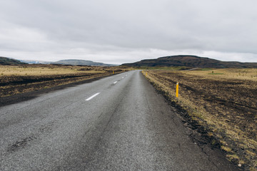 Fototapeta na wymiar The road between the mountains and the hills. Asphalt road in Iceland. The road is in the field.