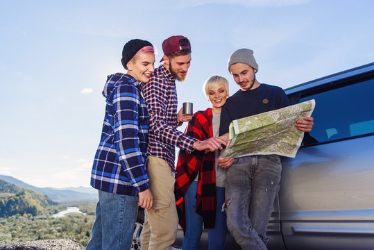 Summer travel concept. Happy friends using map near rented car in nature. Happy hipster travelers planning route together by looking at paper map.