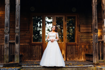 Beautiful young bride in wedding dress stands on porch of wooden
