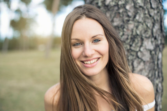 Portrait of smiling young woman leaning against tree trunk
